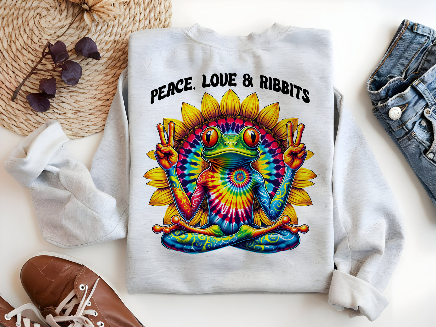 a white sweatshirt with a colorful tie-dye design of a frog, along with the text "Peace. Love. Ribbits" printed on it.