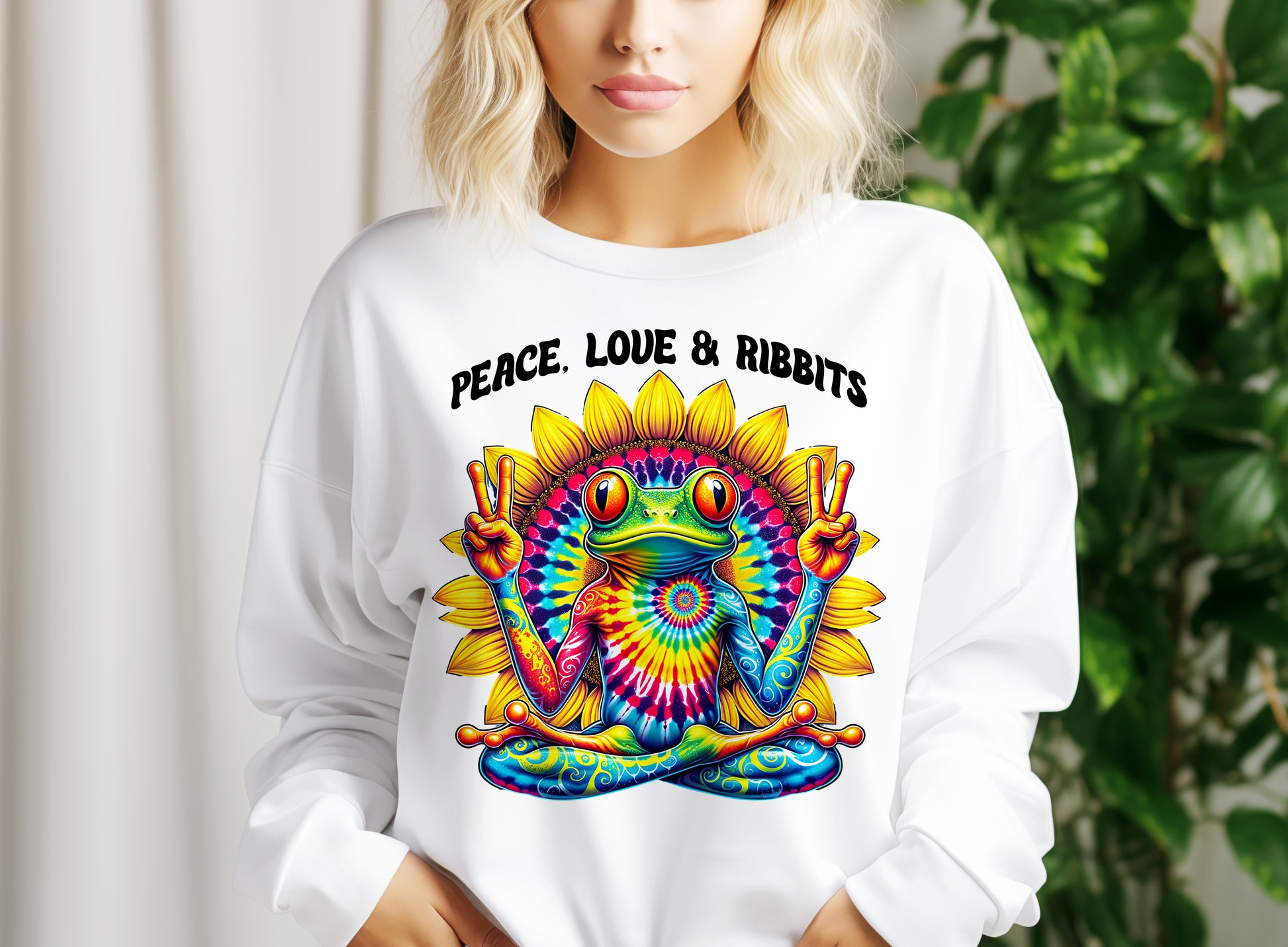 A woman wearing a white sweater with a colorful, tie-dye frog graphic and the text "Peace. Love & Ribbits" printed on it.
