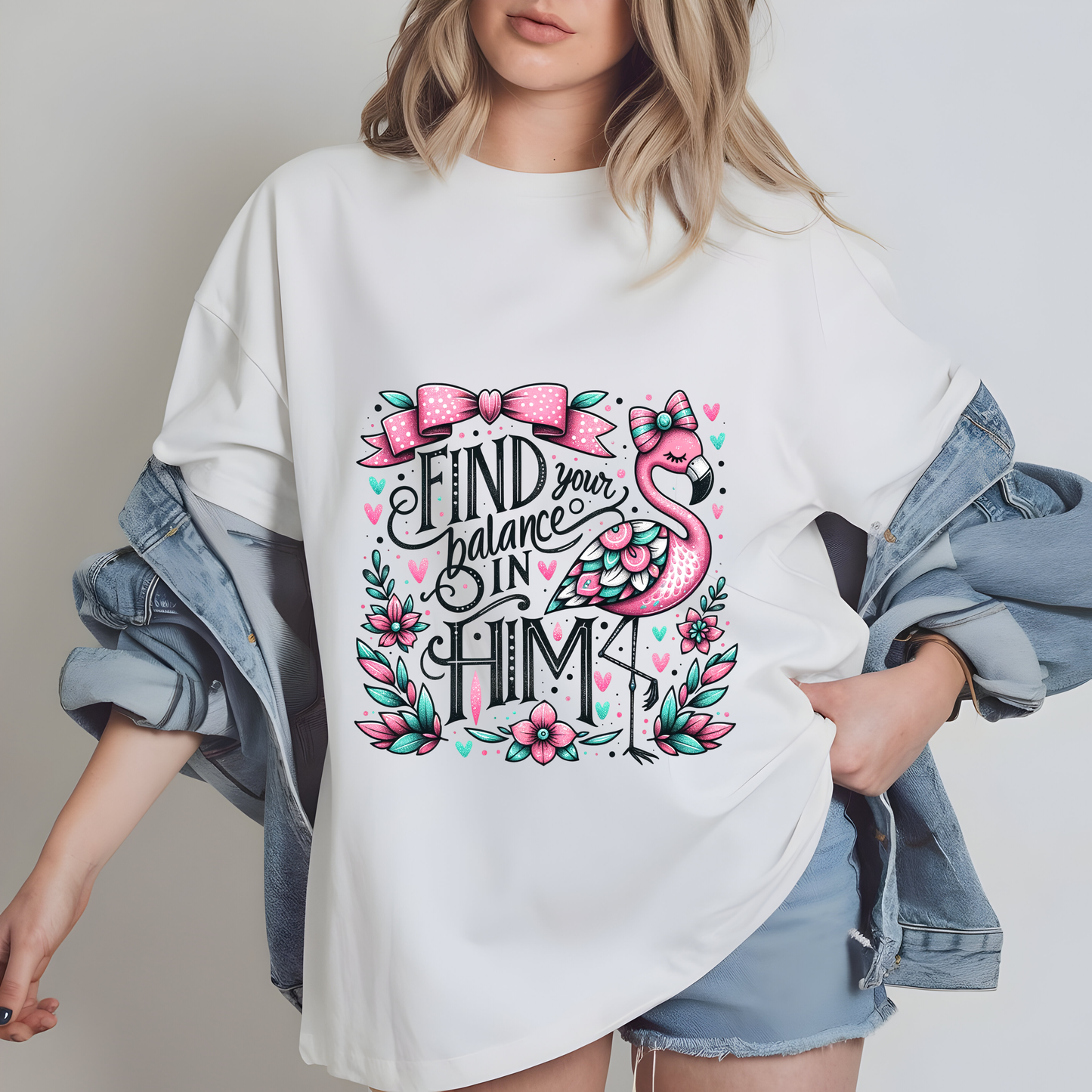 A woman wearing a white t-shirt with a graphic design featuring a pink flamingo and the text "Find your balance in Him" printed on it.