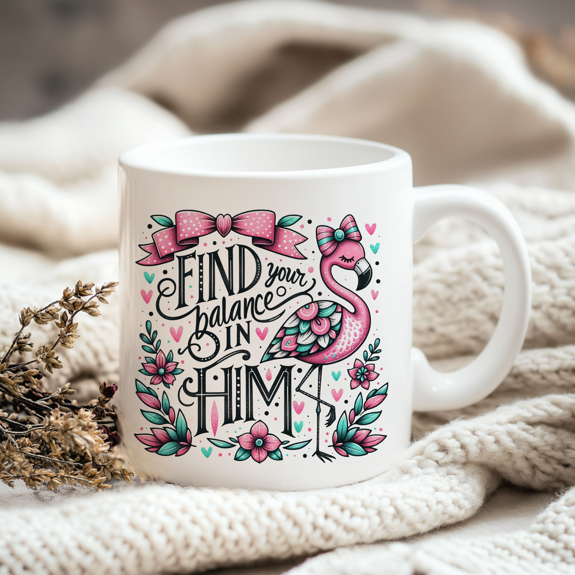 A white ceramic mug with a colorful design featuring a pink flamingo and the text "Find your balance in Him" is placed on a white blanket.