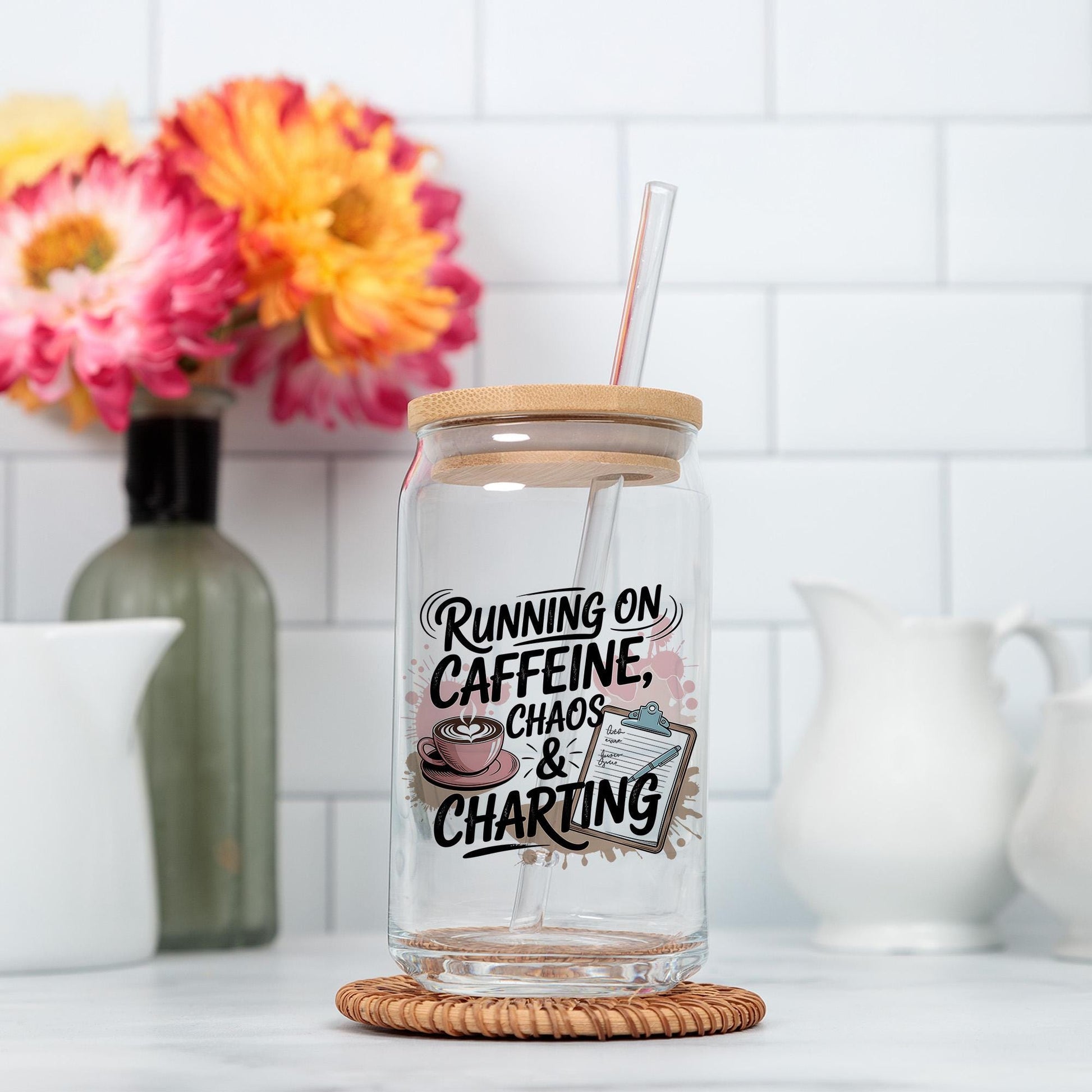 A glass mug with a straw, featuring a humorous text that says "Running on Caffeine, Chaos & Charting". The mug is placed on a coaster, with a vase of colorful flowers in the background.